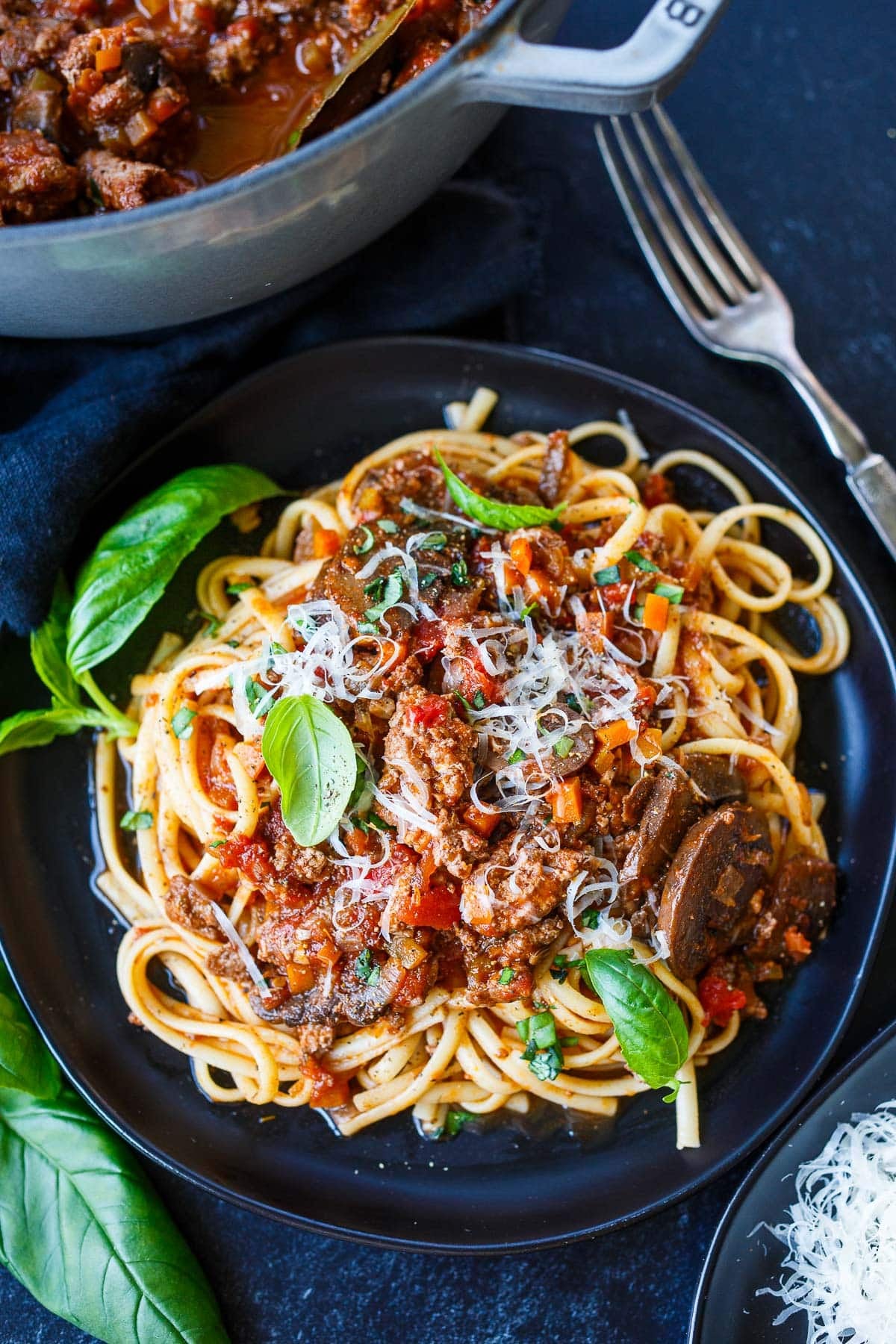 plate of spaghetti topped with turkey bolognese with mushrooms and a garnish of grated Parmesan and fresh basil leaves.