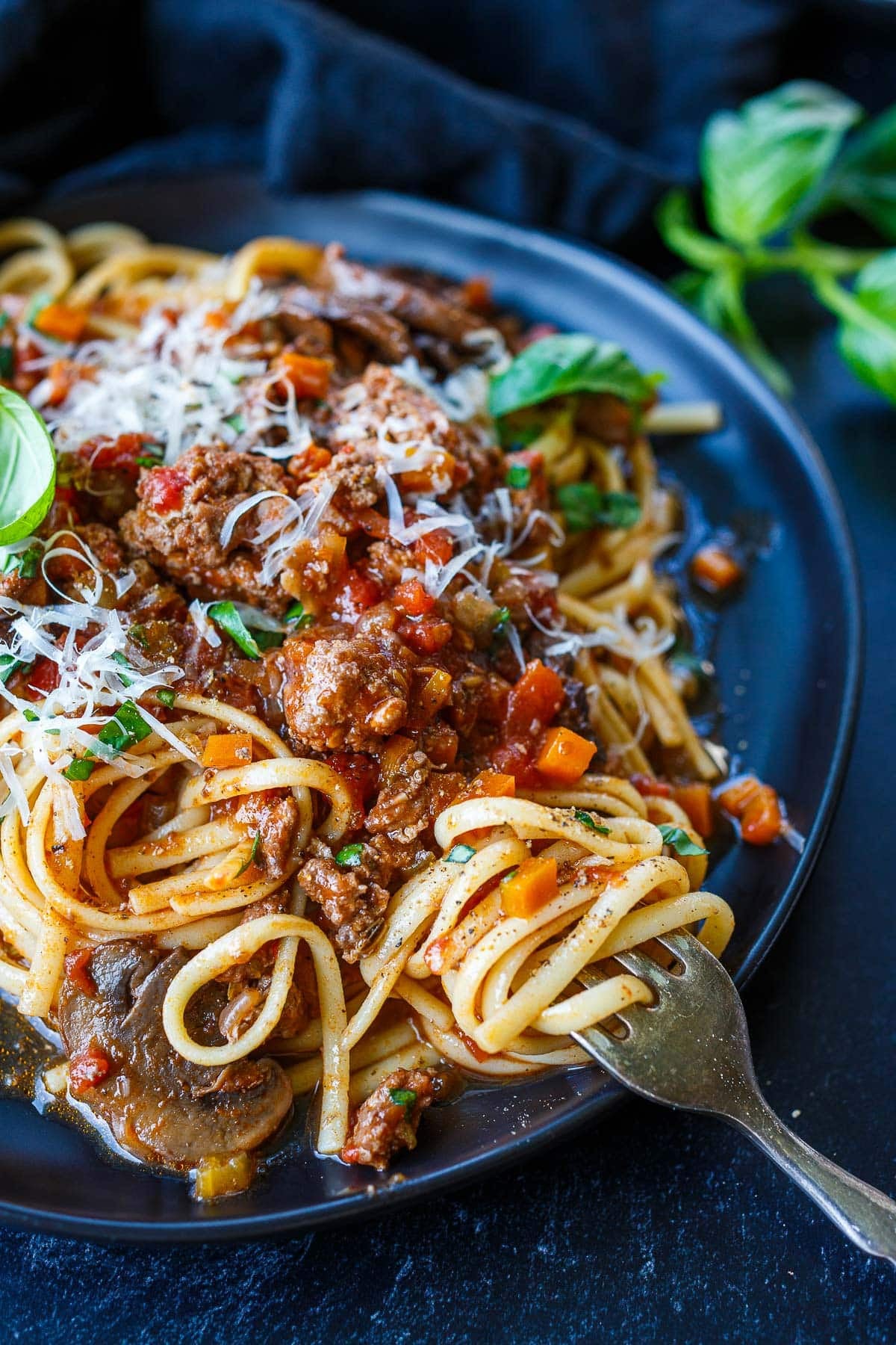 plate of turkey bolognese on spaghetti with grated Parmesan and fresh basil, with a fork twirling the noodles.