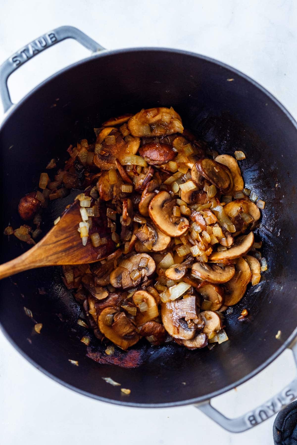sliced cremini mushrooms are sautéing in a Dutch oven.