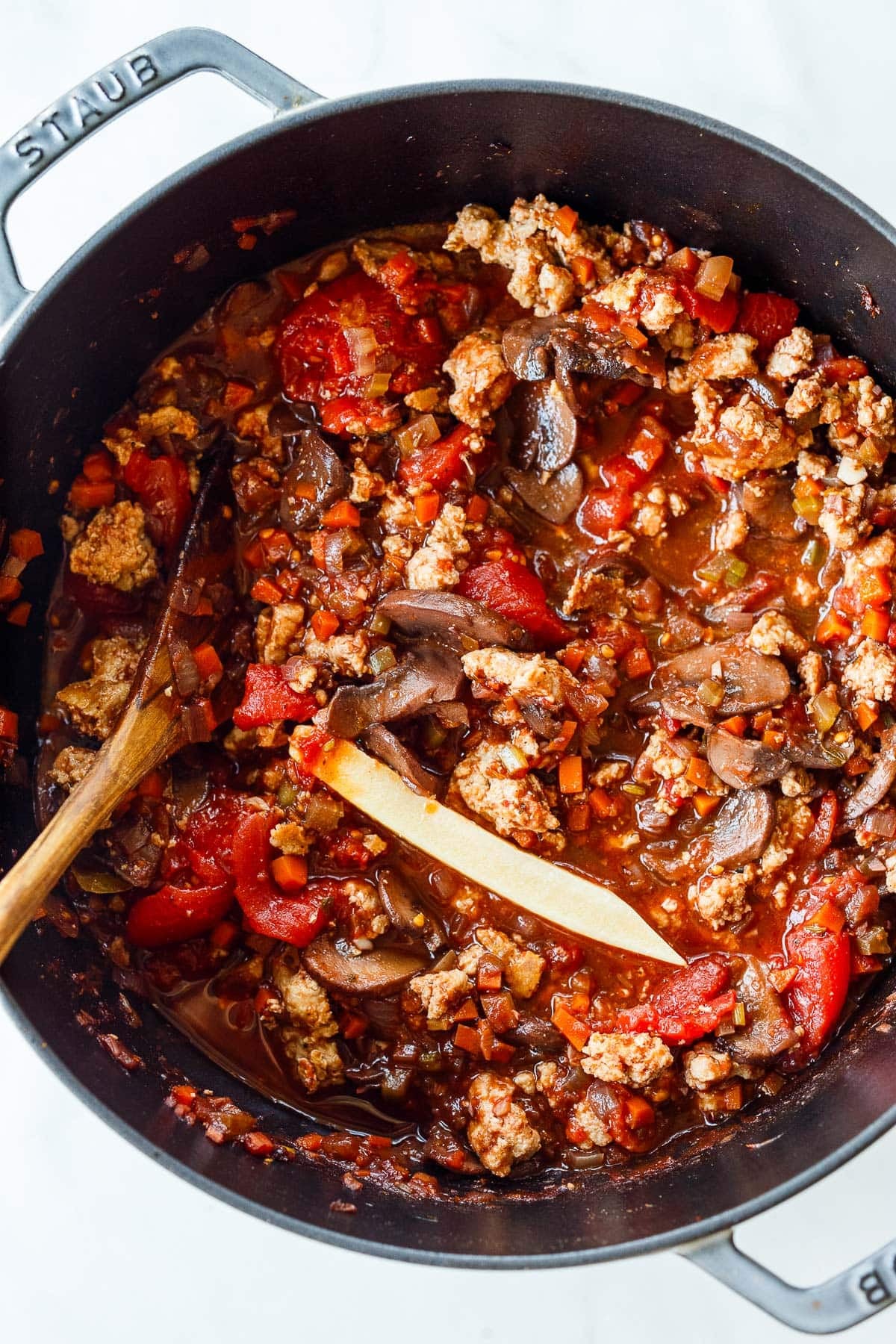 Dutch oven with turkey bolognese sauce simmering with a Parmesan rind.