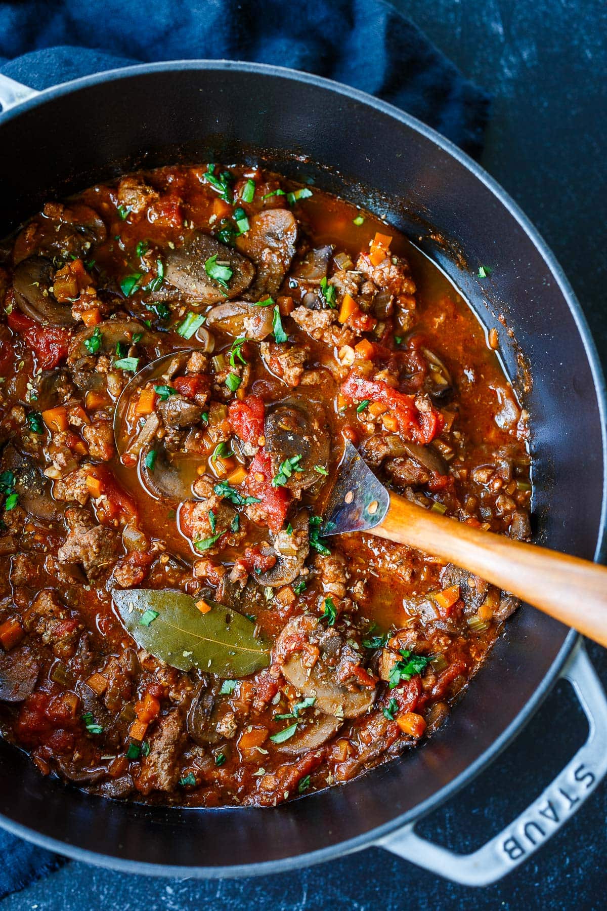 Dutch oven with turkey bolognese sauce with mushrooms, bay leaf, and fresh parsley, with serving utensil.