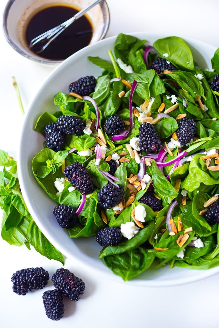 A refreshing Blackberry Salad with crumbled goat cheese, and toasted almonds with a simple balsamic vinaigrette, in a white bowl. 
