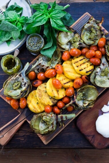 Grilled Artichokes and Polenta with Blistered tomatoes, pesto, capers and fresh basil-- served family style ...perfect for a casual summer evening! Vegan and GF | www.feastingathome.com| #grilledartichokes