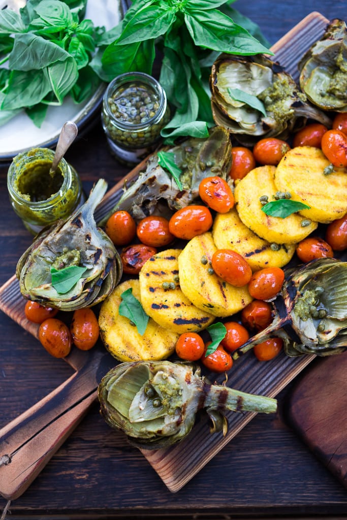 Grilled Artichokes and Polenta with Blistered tomatoes, pesto, capers and fresh basil-- served family style ...perfect for a casual summer evening! Vegan and GF | www.feastingathome.com| #grilledartichokes