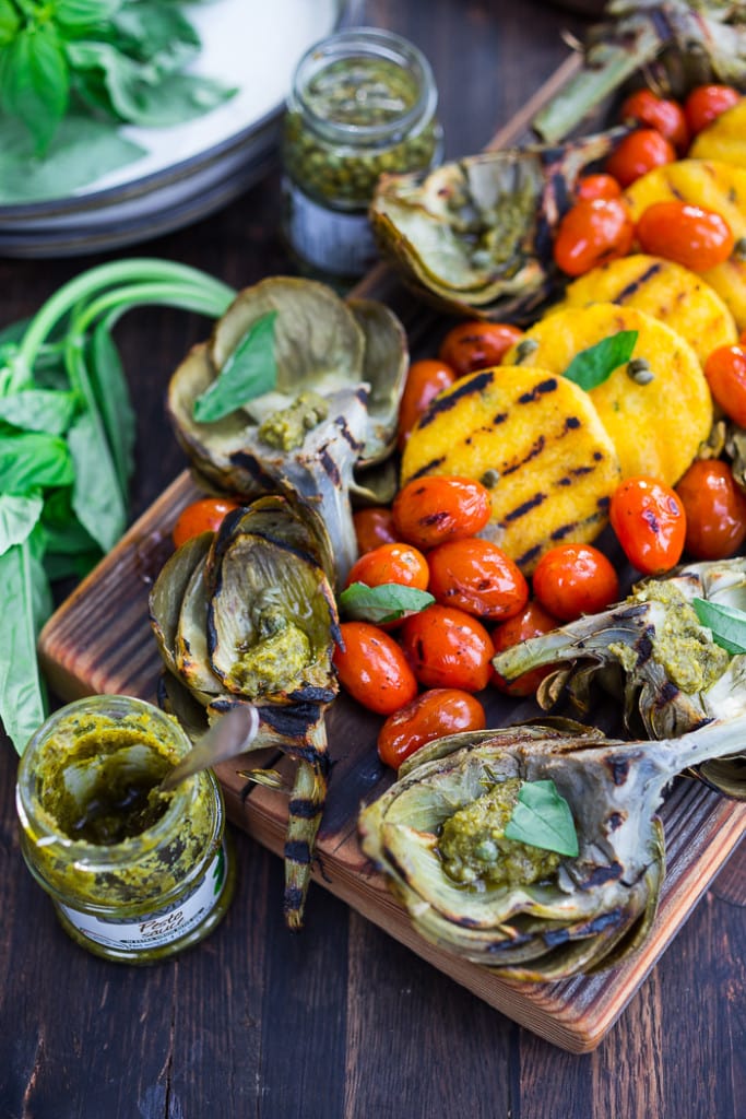 Grilled Artichokes and Polenta with Blistered tomatoes, pesto, capers and fresh basil-- served family style ...perfect for a casual summer evening! Vegan and GF | www.feastingathome.com| #grilledartichokes