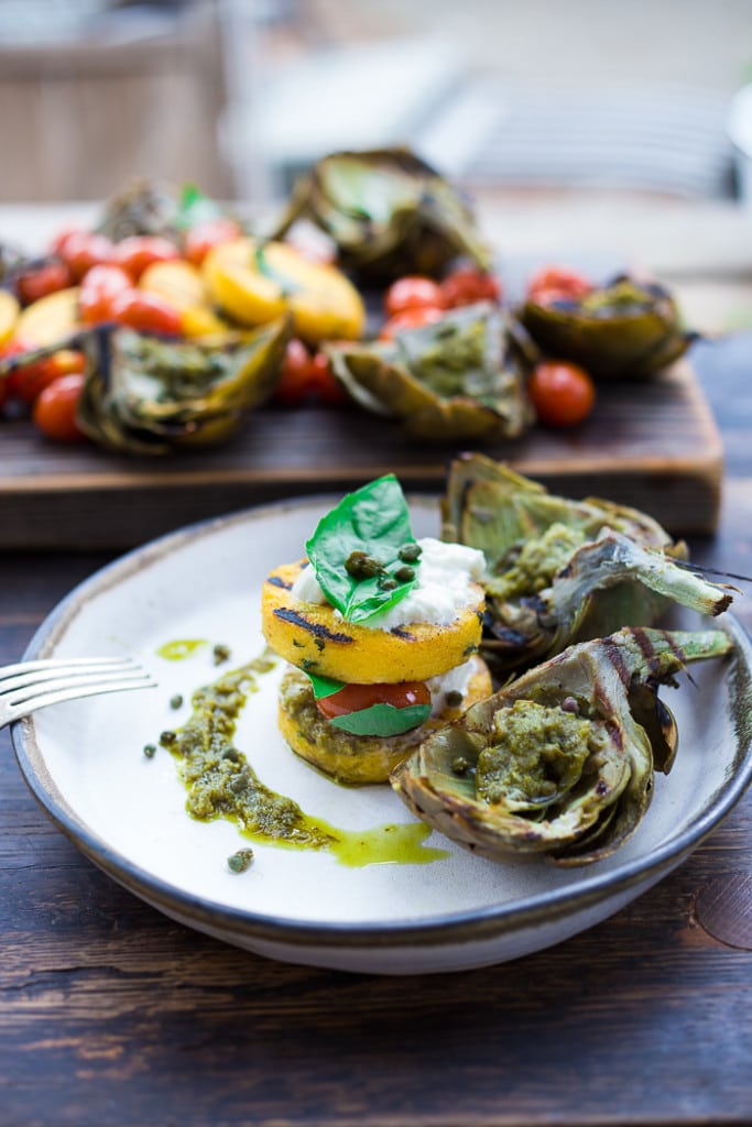 Grilled Artichokes and Polenta with Blistered tomatoes, pesto, capers and fresh basil-- served family style ...perfect for a casual summer evening! Vegan and GF | www.feastingathome.com| #grilledartichokes