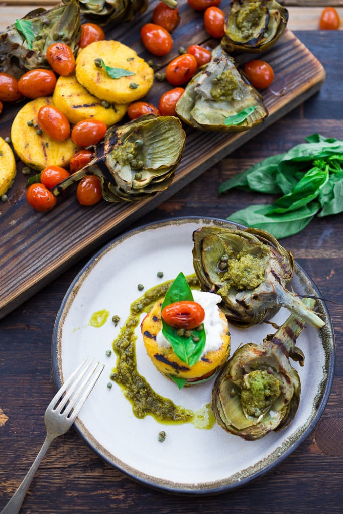 Grilled Artichokes and Polenta with Blistered tomatoes, pesto, capers and fresh basil-- served family style ...perfect for a casual summer evening! Vegan and GF | www.feastingathome.com| #grilledartichokes
