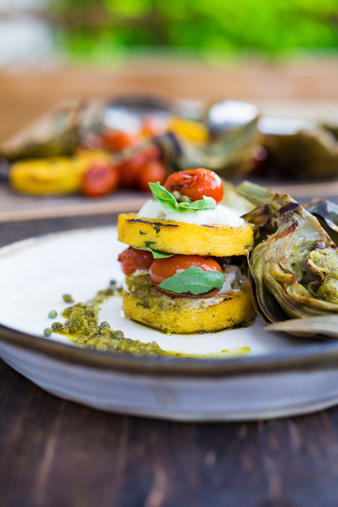 Grilled Artichokes and Polenta with Blistered tomatoes, pesto, capers and fresh basil-- served family style ...perfect for a casual summer evening! Vegan and GF | www.feastingathome.com| #grilledartichokes