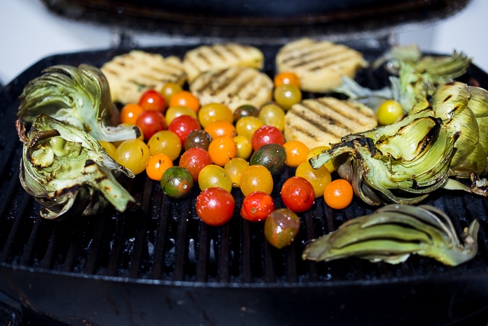 Grilled Artichoke and Polenta with blistered tomatoes, pesto, capers and fresh basil -served family style! An easy healthy rustic meal, perfect for summer nights on the patio! Vegan and GF | www.feastingathome.com| #grilledartichokes #artichokes #grilled #easy #vegan 