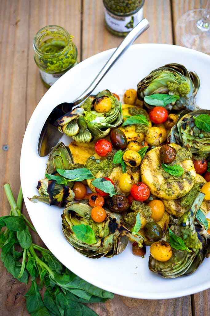 Grilled Artichokes and Polenta with Blistered tomatoes, pesto, capers and fresh basil-- served family style ...perfect for a casual summer evening! Vegan and GF | www.feastingathome.com| #grilledartichokes