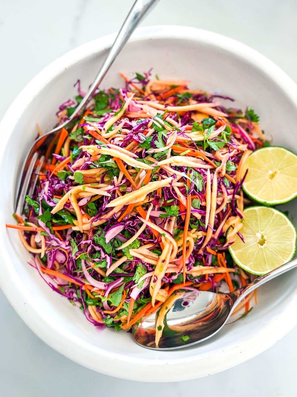 mango salad in a bowl with limes and cabbage.
