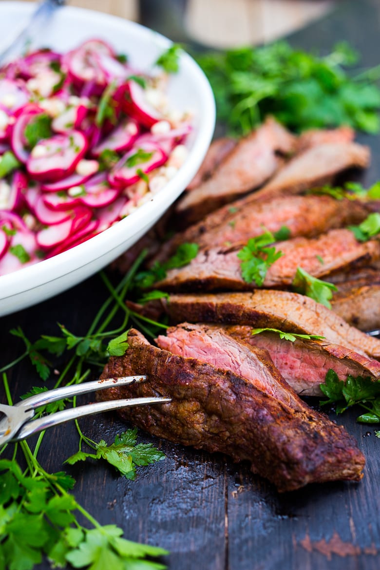 slices of grilled flank steak recipe on a wood board with cilantro.