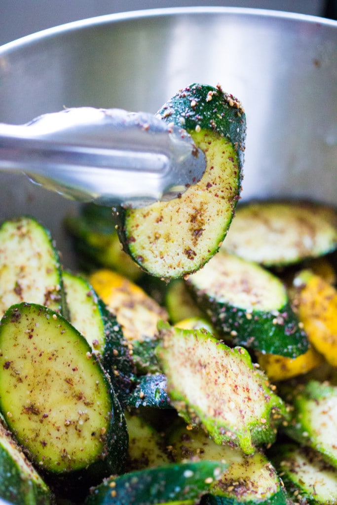Tossing zucchini with olive oil and spices in a bowl.