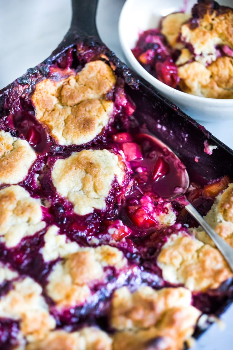 This Peach Skillet Cobbler is topped with a golden and delicious, biscuit topping with fresh summer peaches and berries. This can be made gluten-free and or vegan! #peachcobbler #skilletcobbler #summer #desserts #peachdesserts #huckleberries #vegancobler #glutenfreecobbler #vegandessert 