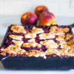How to make skillet cobbler with fresh summer peaches and optional huckleberries. Use other summer berries, like black berries or blueberries! This can be made gluten-free and or vegan!