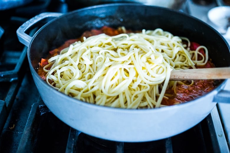 Spaghetti being added to tomato sauce.