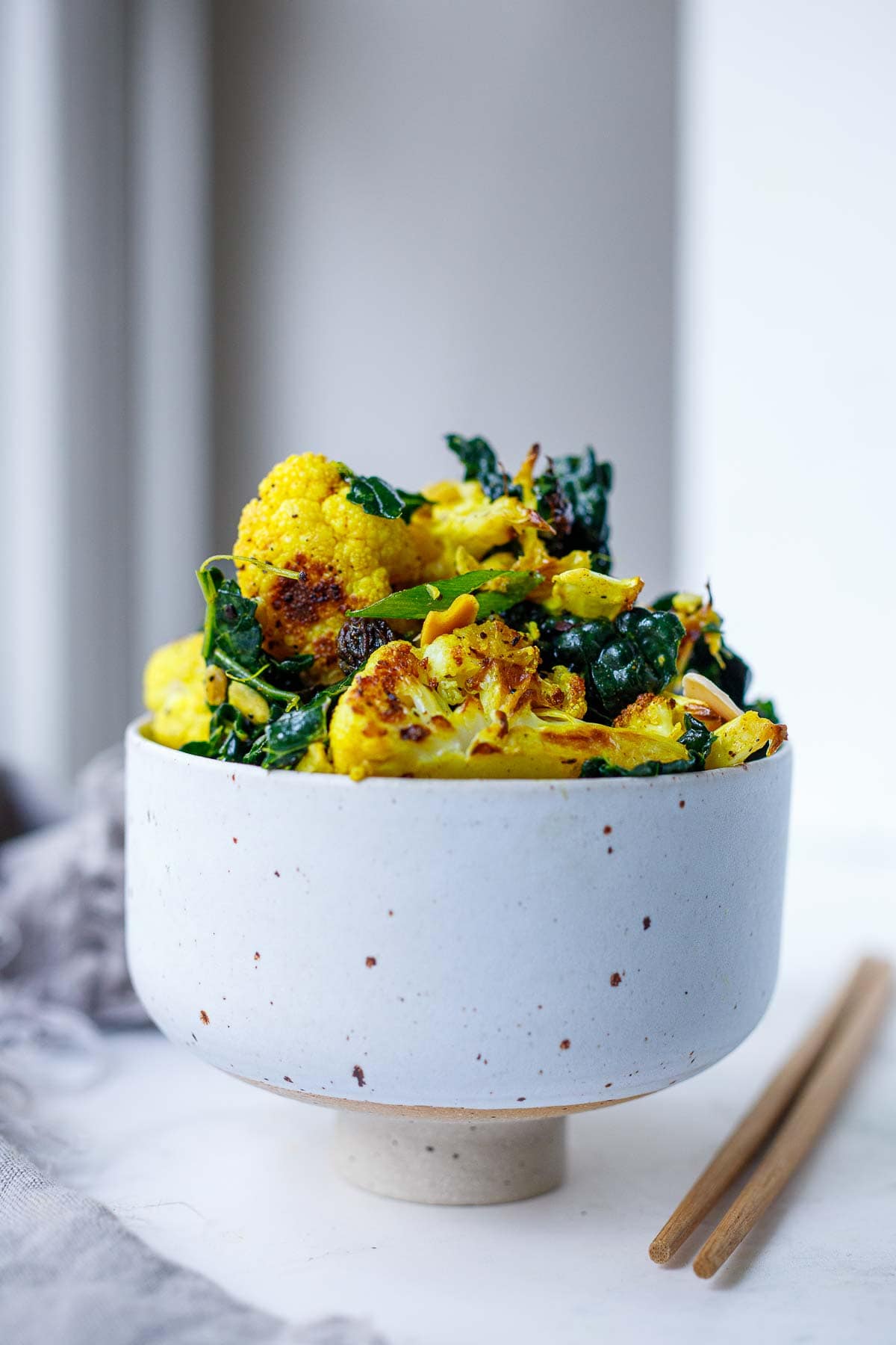 This Roasted Cauliflower Salad recipe is incredibly flavorful. Cauliflower is roasted until tender-crisp, then tossed with farro, lacinato kale, scallions, raisins, and toasty almonds in a savory-sweet turmeric dressing. Vegan. 