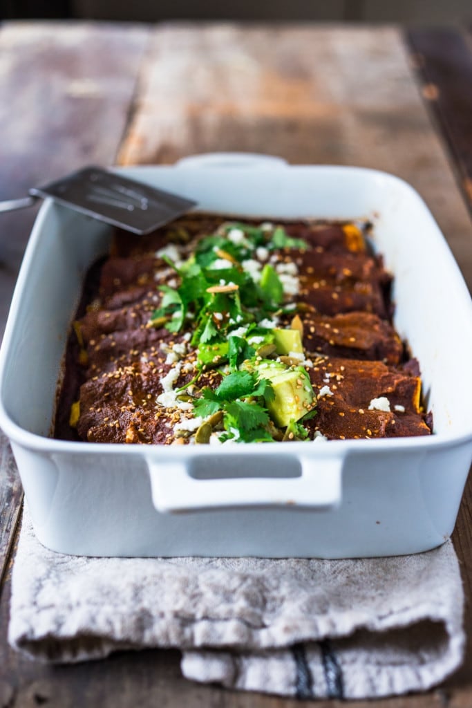 butternut squash enchiladas in ceramic baking dish with mole sauce, avocado, and cilantro.