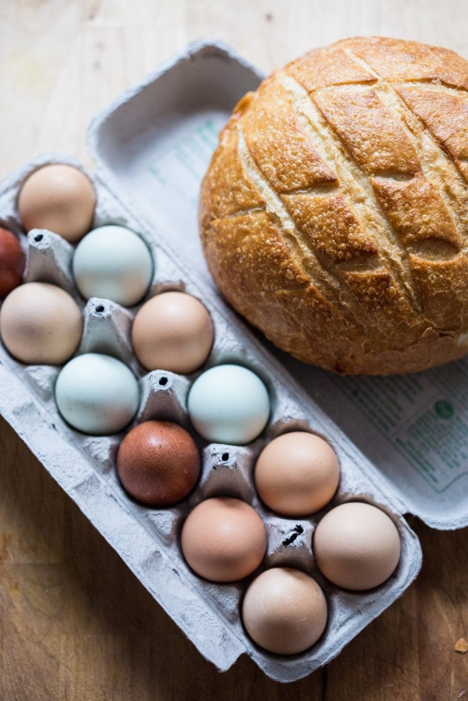 a loaf of sourdough bread next to fresh eggs on a wood countertop, for making breakfast strata. 