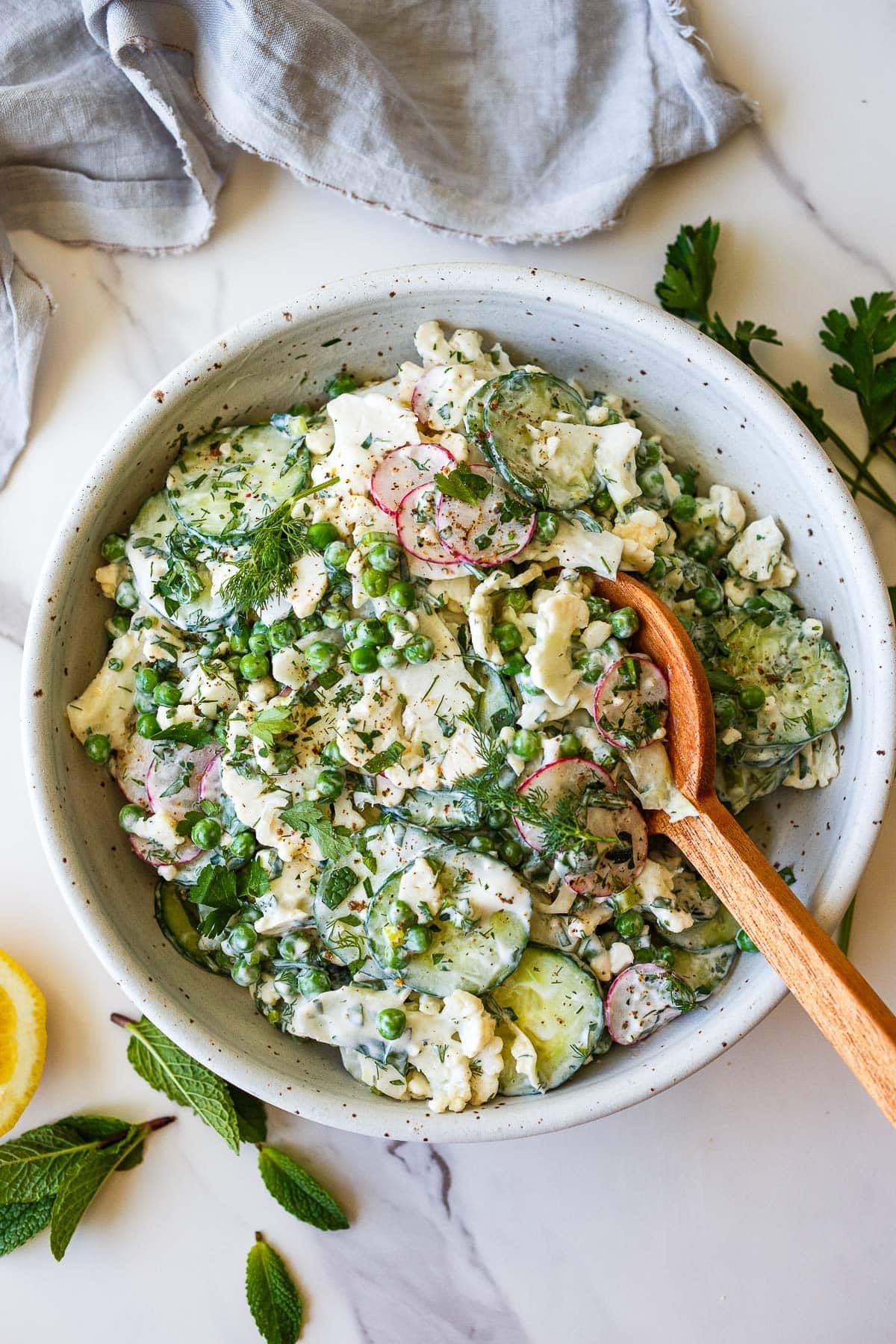 cauliflower salad with creamy yogurt dressing in salad bowl with wood serving spoon, with peas, dill, radish, cucumber.