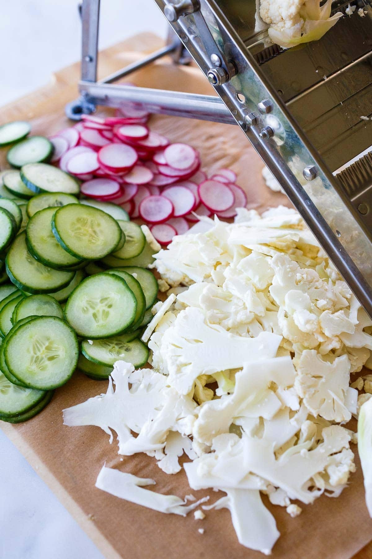 mandolin on wood cutting board with shaved cauliflower, cucumber, and radish.