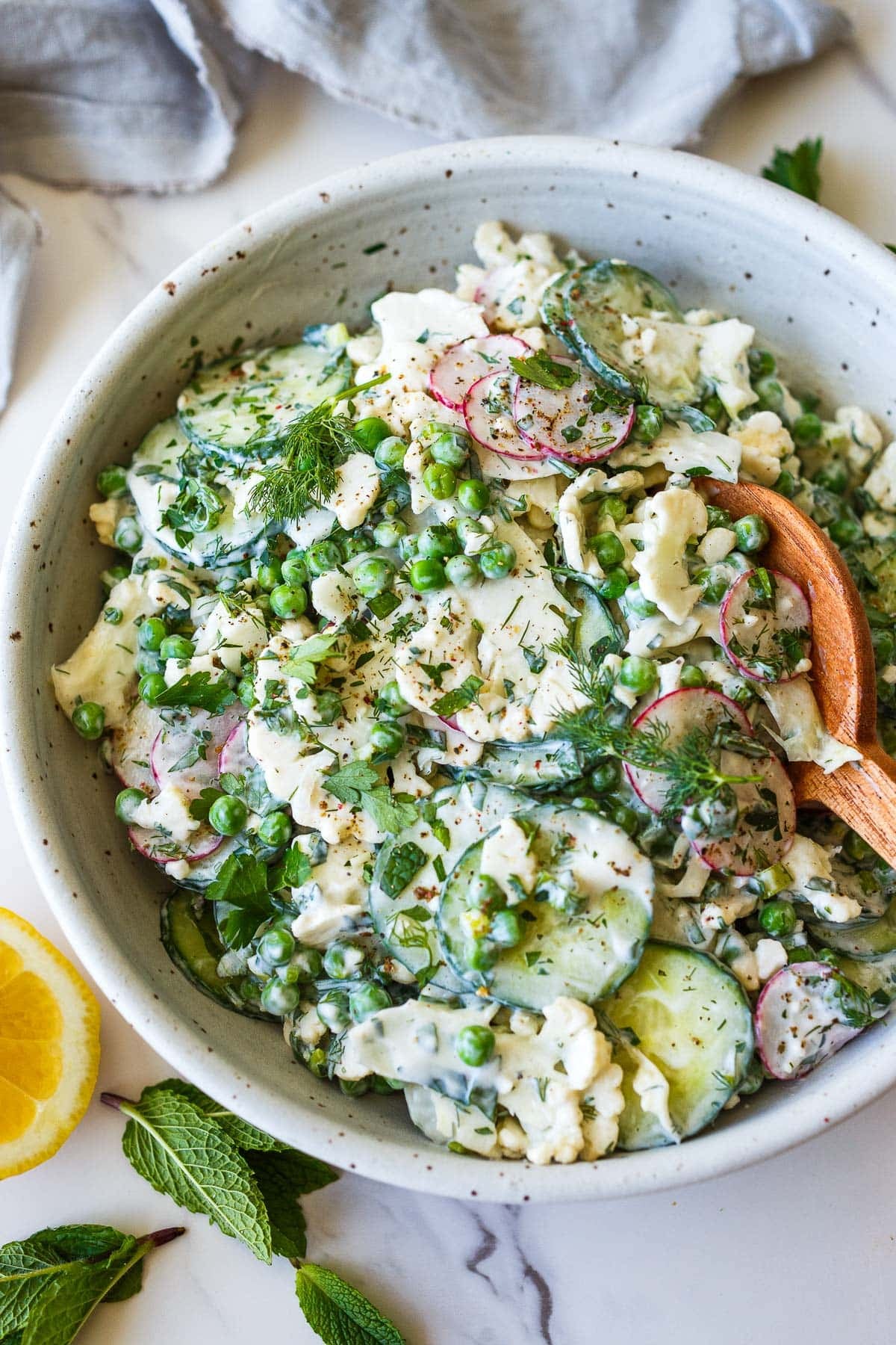 cauliflower salad with peas, dill, radish, and cucumber, in salad bowl with wood spoon.