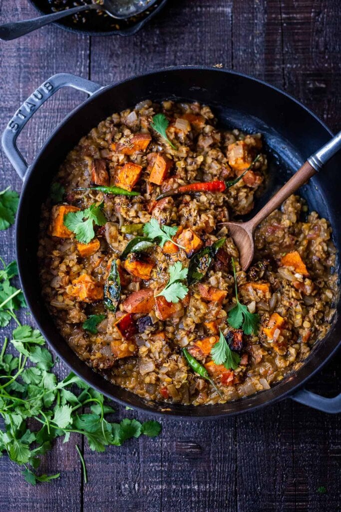 braiser with lentil dal with sweet potatoes, topped with fresh cilantro, with a wooden serving spoon. 