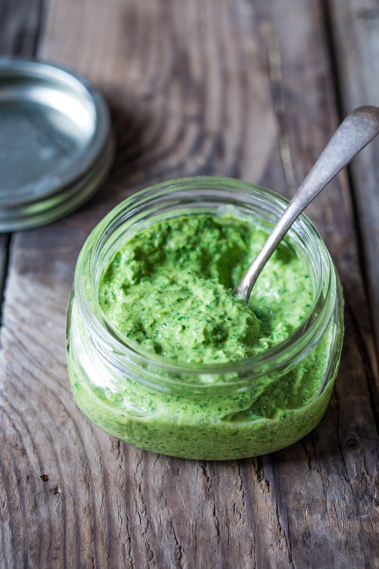 small and wide jar of green harissa sauce with spoon. 