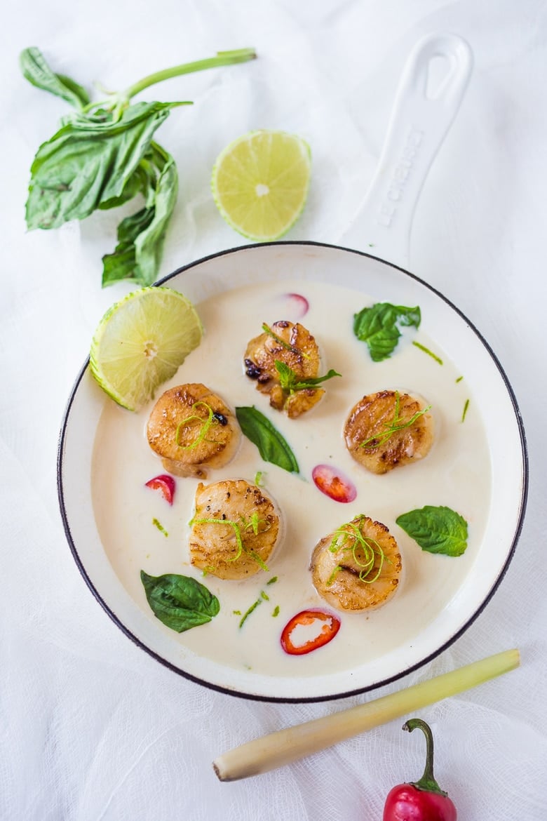 Thai-inspired seared scallops with a coconut-lemongrass sauce in a white pan with tahi basil and lime.