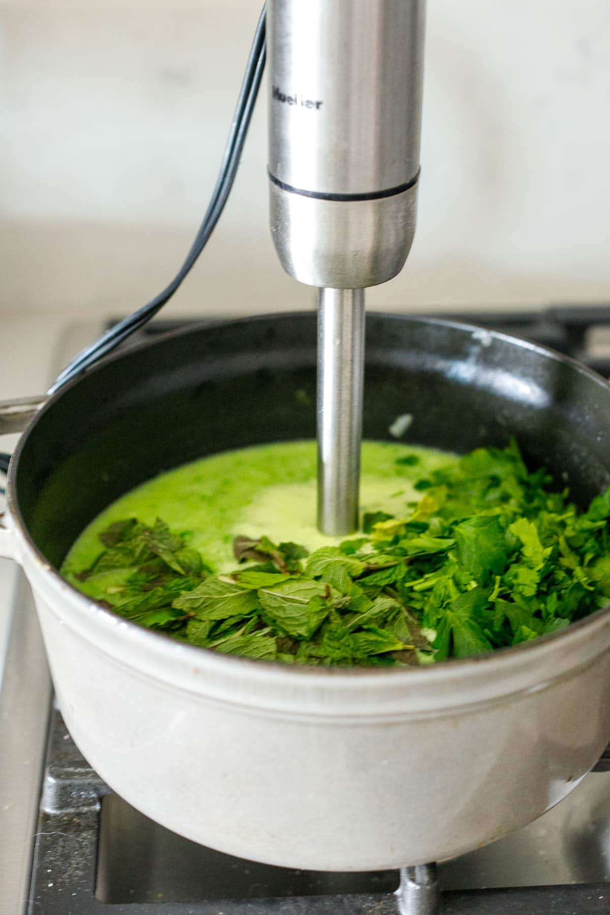 pea soup with fresh mint and parsley being blended in with an immersion blender.