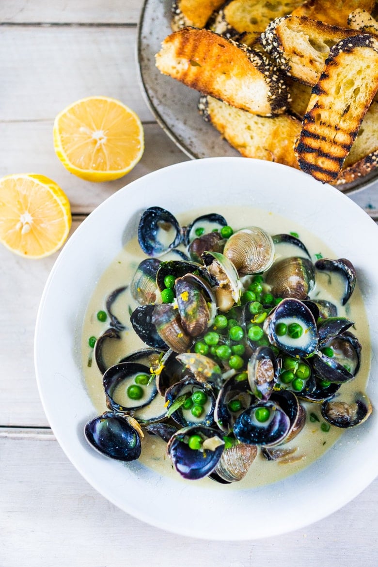 Steamed Clams in a flavorful French-style ,Tarragon White Wine Broth with fresh peas, served with crusty bread to mop up all the flavorful juices! 