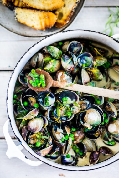 Steamed Clams in a flavorful French-style ,Tarragon White Wine Broth with fresh peas, served with crusty bread to mop up all the flavorful juices!