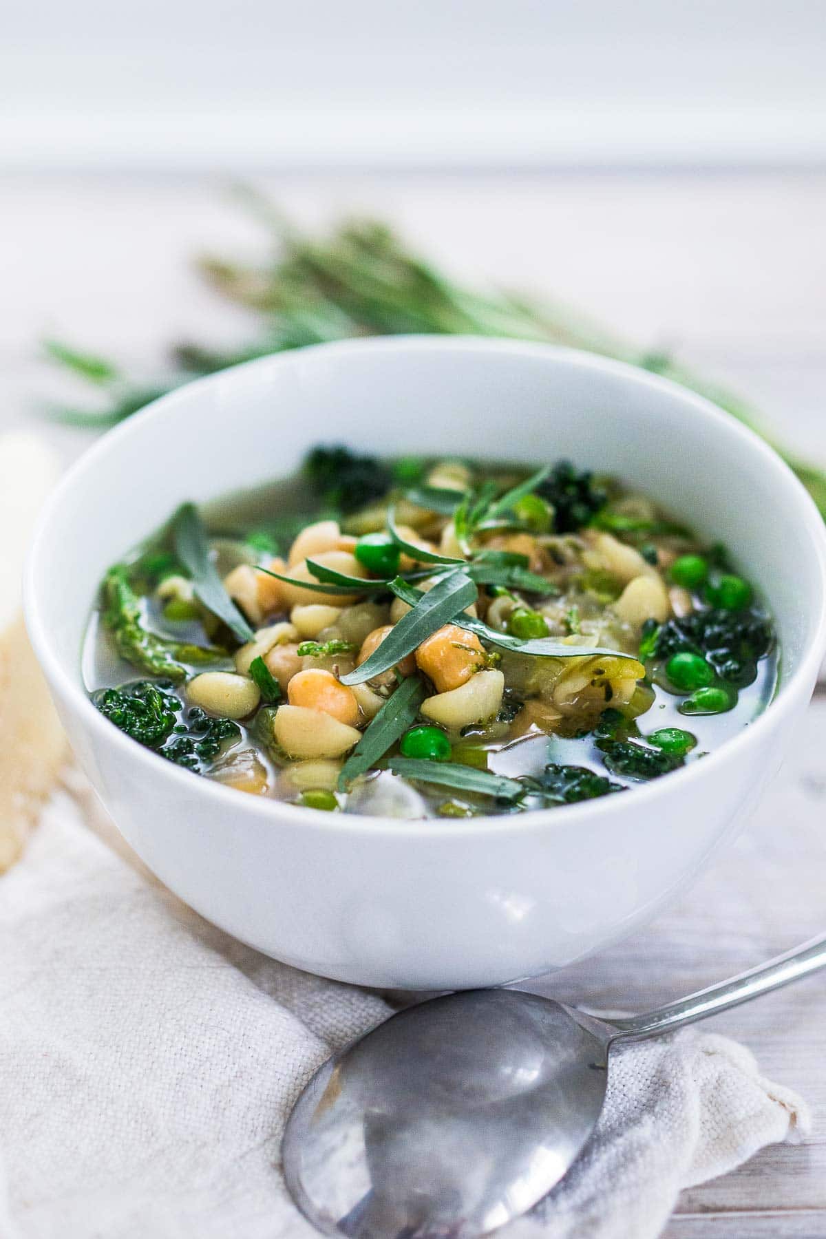 bowl of spring minestrone soup with chickpeas, garnished with fresh tarragon.