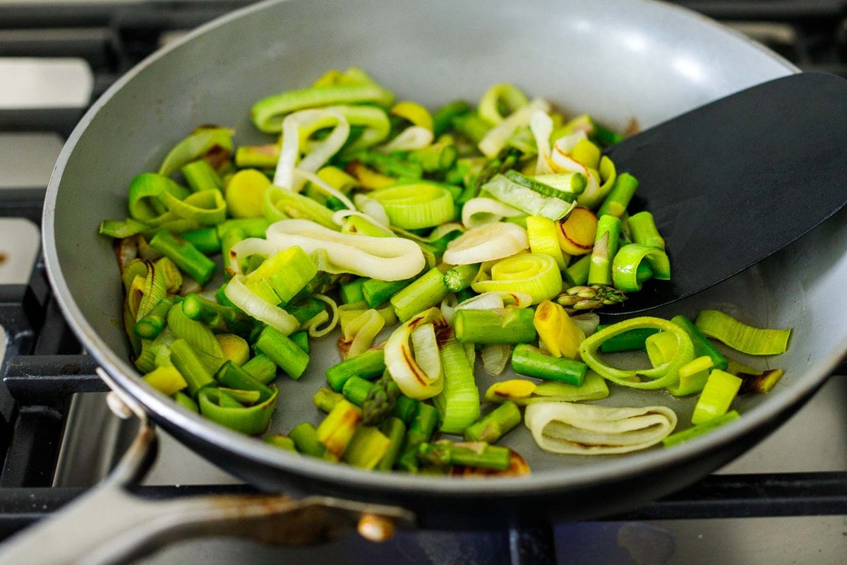 sauteing leeks and asparagus in a pan.