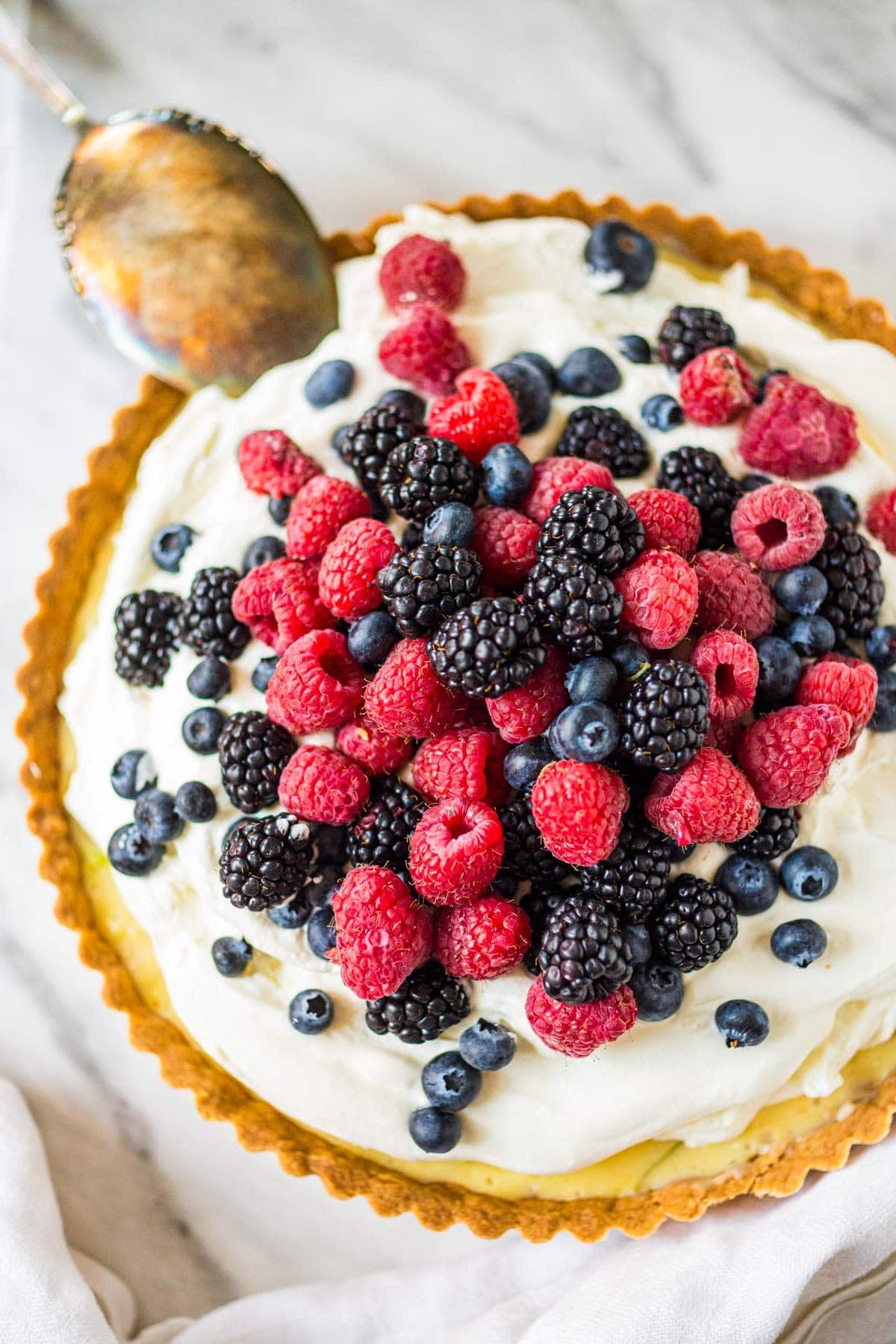 This irresistible Summer Berry Tart recipe features fresh, juicy summer berries over a creamy, lemony filling, vanilla whipped cream, and a buttery shortbread crust.