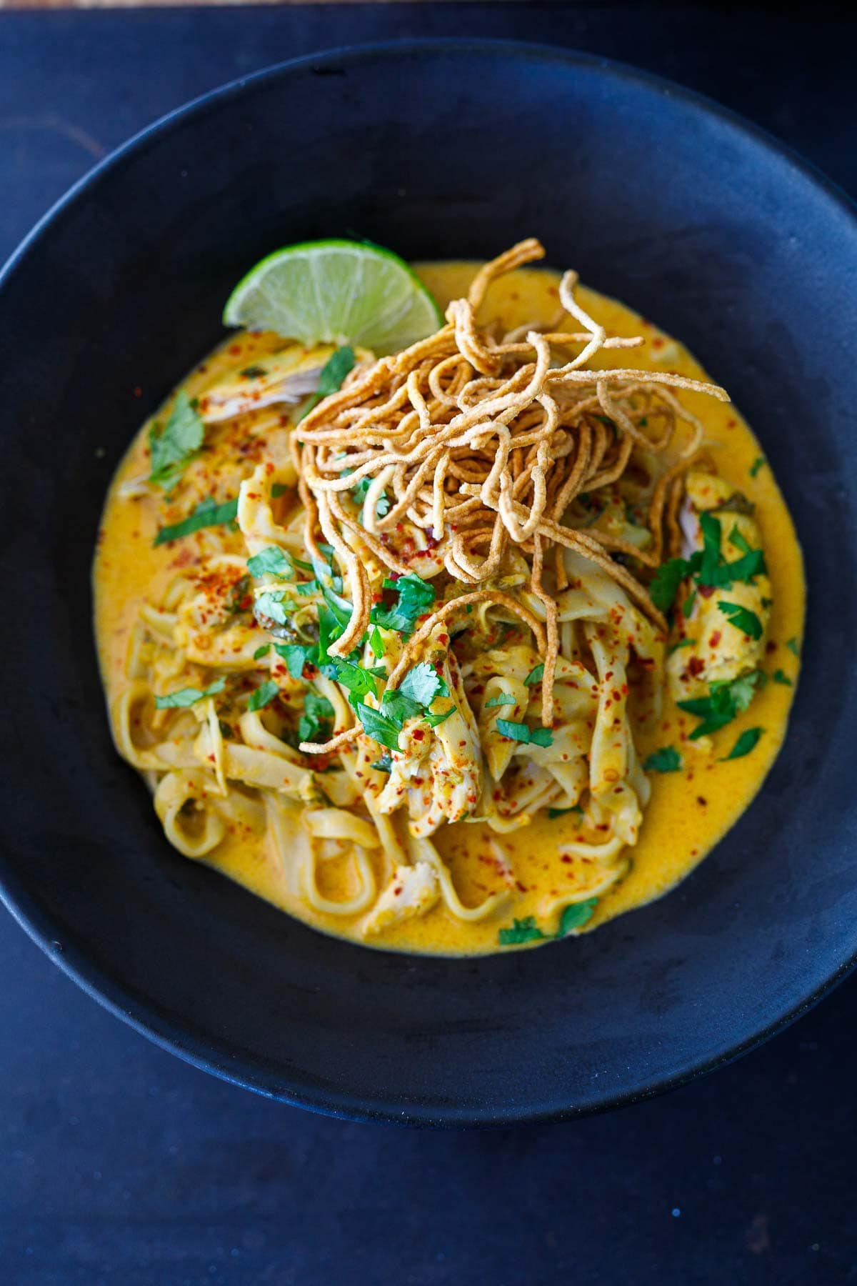 Khao Soi recipe in a black bowl with a lime and cripsy noodles. 