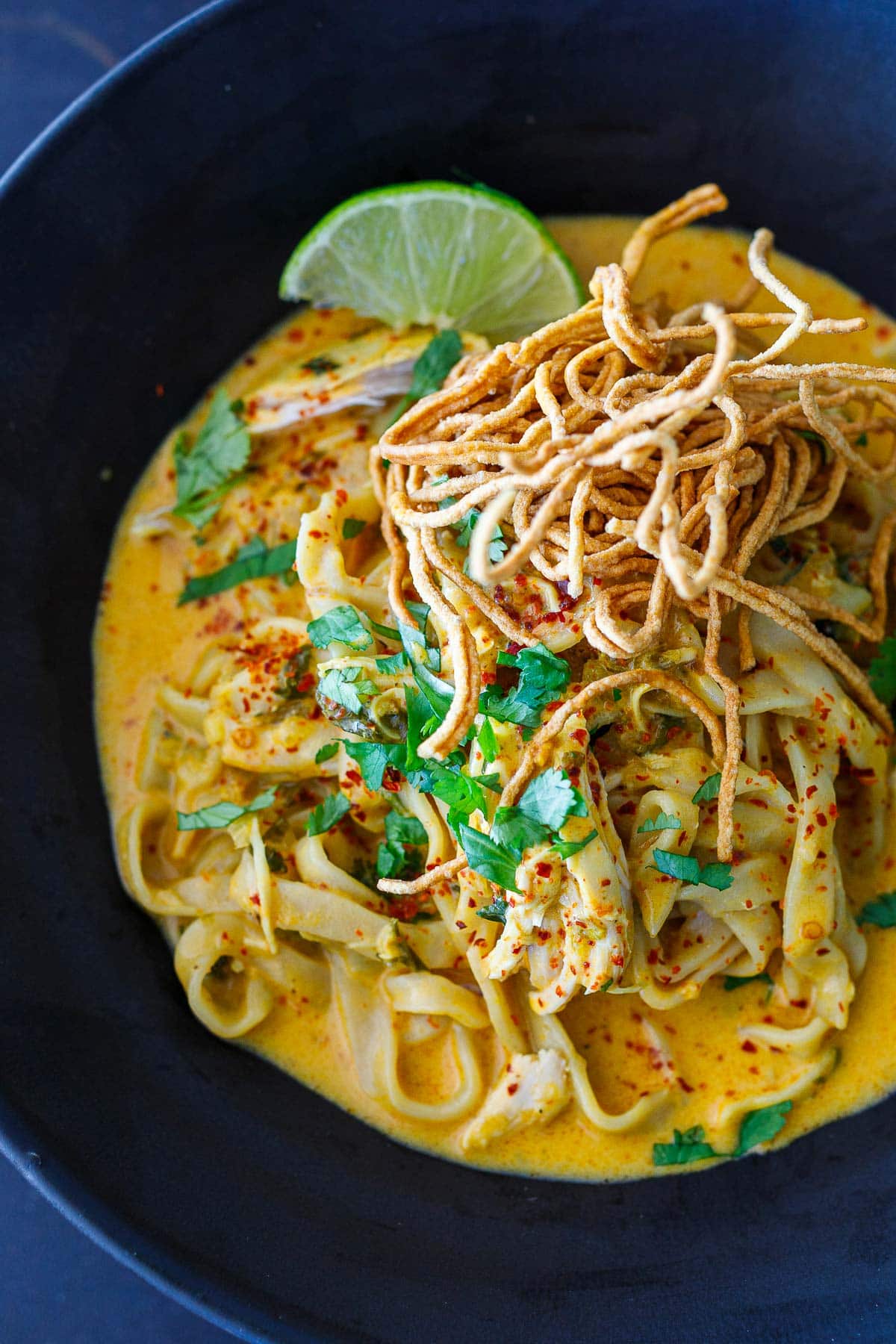 Khao Soi in a black bowl with crispy noodles and pickled mustard greens. 