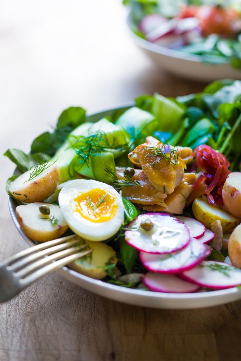 A Scandinavian twist on the classic nicoise salad - Nordic Nicoise Salad is made with smoked fish ( salmon, trout, sardines) or pickled herring, on a bed of watercress, with radish, cucumber ribbons, baby potatoes, capers, dill, chive blossoms and horseradish-spiked nicoise dressing. Fresh and tasty! | www.feastingathome.com