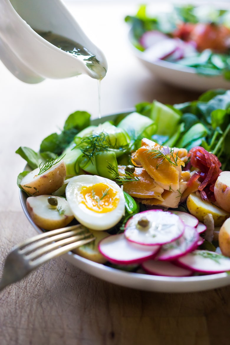 A Scandinavian twist on the classic nicoise salad - Nordic Nicoise Salad is made with smoked fish ( salmon, trout, sardines) or pickled herring, on a bed of watercress, with radish, cucumber ribbons, baby potatoes, capers, dill, chive blossoms and horseradish-spiked nicoise dressing. Fresh and tasty! | www.feastingathome.com