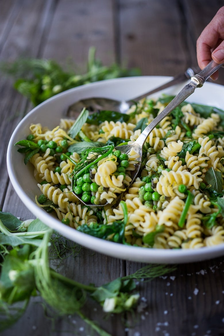 serving spoon lifting pea pasta from serving bowl- spring pea pasta with herbs and pea shoots.