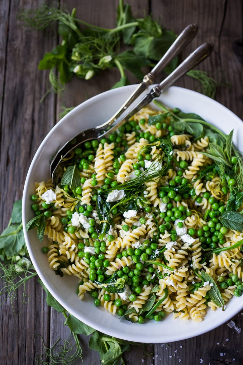 serving bowl with spring pea pasta with lemon zest, fresh herbs, english peas, goat cheese crumbles, and truffle oil.