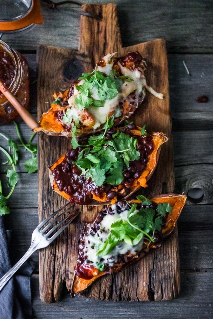 stuffed sweet potatoes with bbq beans, cheese, and cilantro on a wood plank.