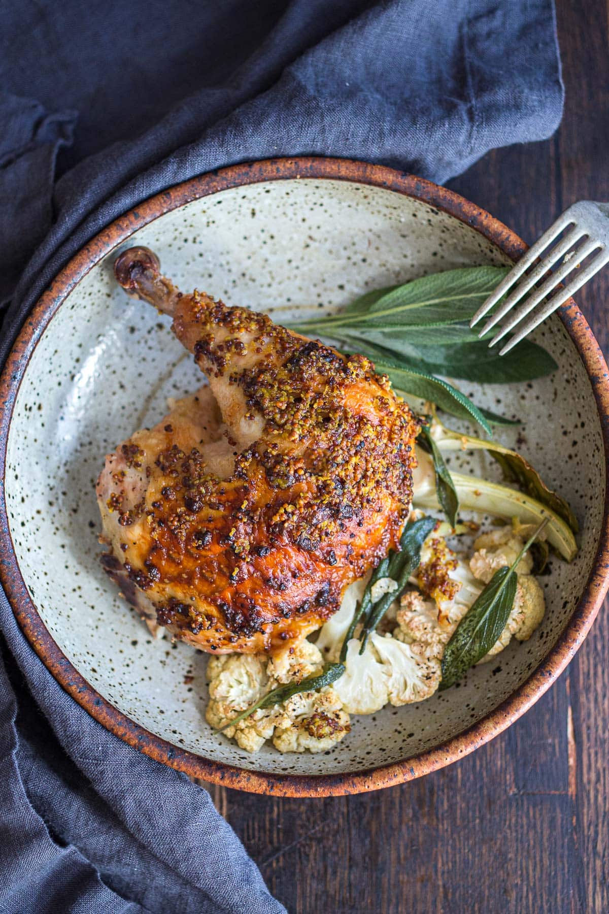 Spatchcock chicken in a serving bowl with roasted cauliflower and sage. 