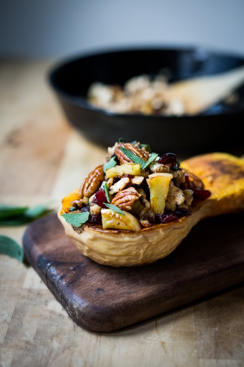 stuffed butternut squash recipe filled with pecans, apples, dried cranberries, and sage on wood board.