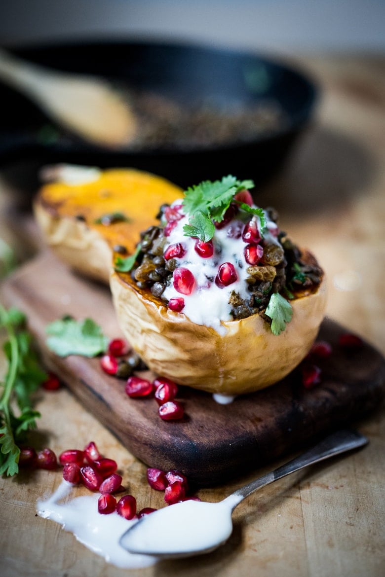 stuffed butternut squash recipe with lentils, golden raisins, yogurt, pomegranate seeds, and parsley on wood board with spoon resting in front with yogurt.