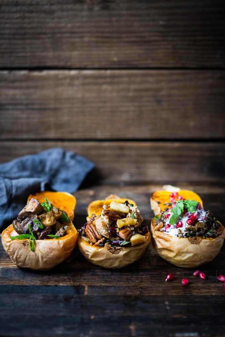 three stuffed butternut squash halves, one with miso mushrooms and tofu, one with pecans, apples, and turkey, and one with lentils, yogurt, and pomegranate.