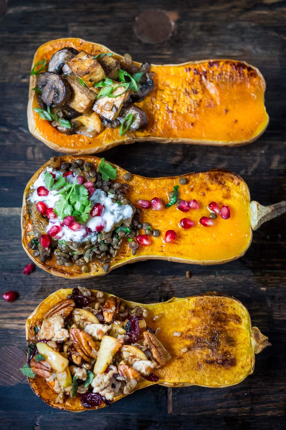 three roasted butternut squash halves stuffed with different fillings - mushrooms and tofu, lentils and yogurt, and pecans, apples, and cranberries.