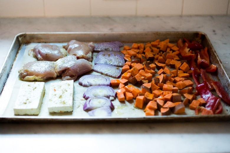 raw chicken, tofu, onions and veggies on a sheet pan