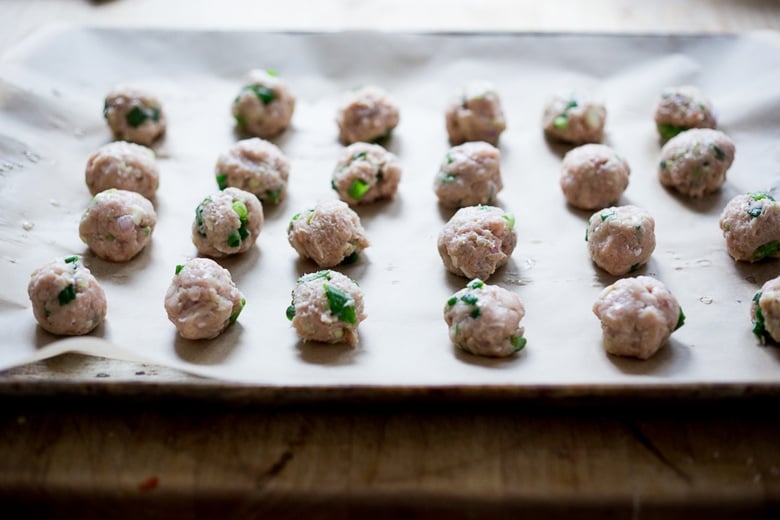 baking sheet with parchment paper with chicken meatballs arranged evenly on the pan.