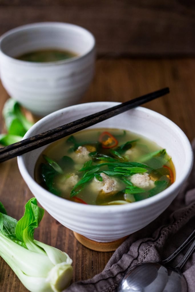 brothy bowl of chicken meatball soup with fresh greens and chilies.